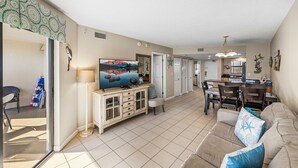 Un salón amplio con una televisión de pantalla plana grande, una zona de comedor y una cocina al fondo.