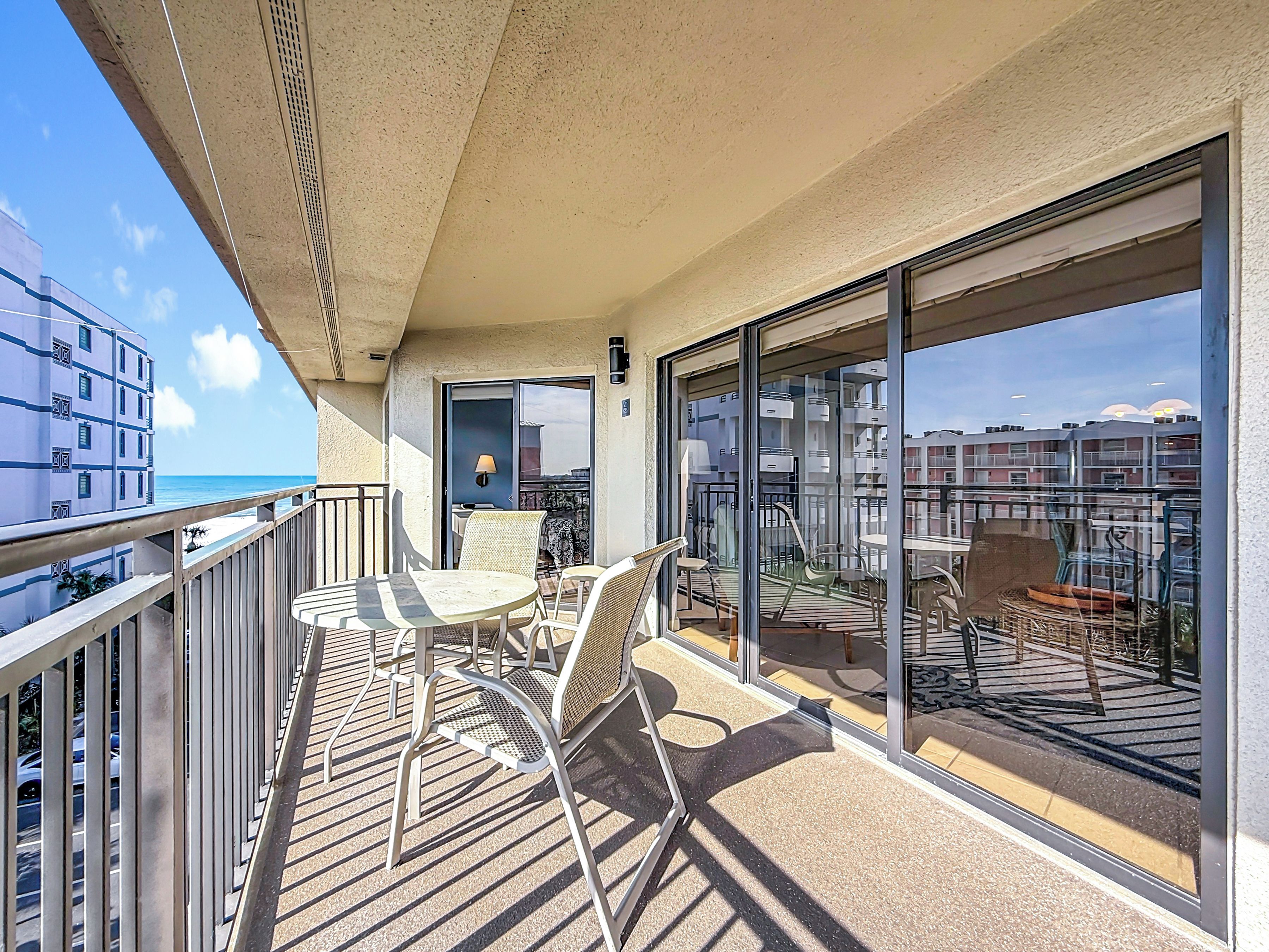 A balcony with a table and chairs, a view of the sea, and a building in the background.