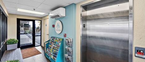 Un ascensor con detalles metálicos, un reloj de pared y un mueble con revistas.