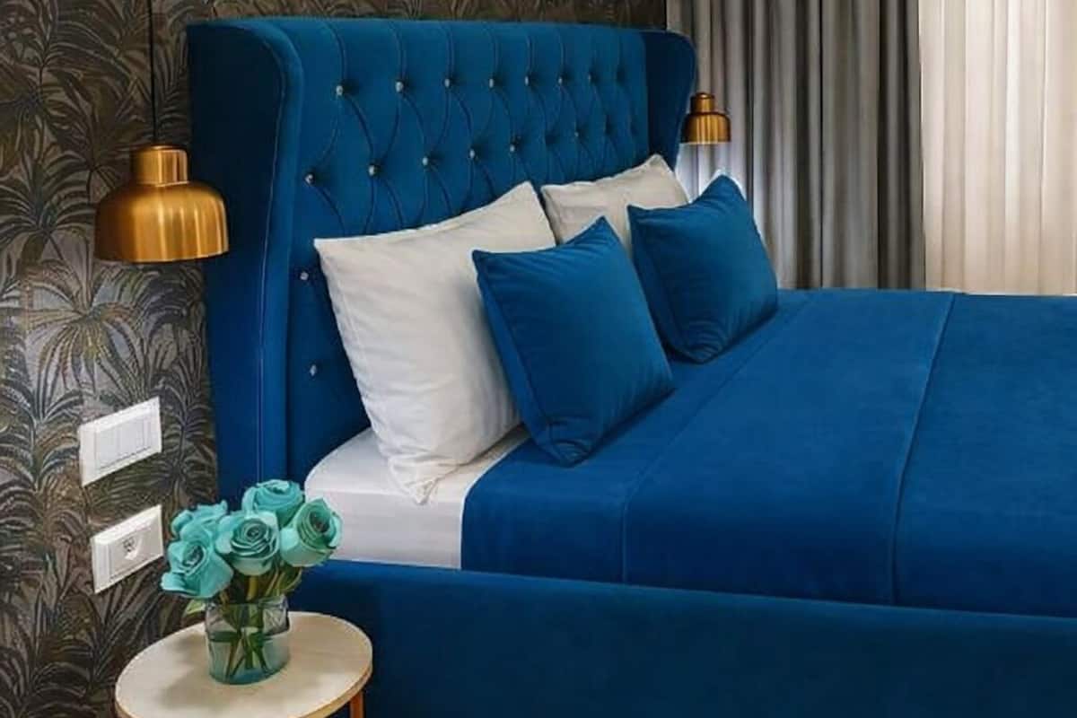 Ein Schlafzimmer mit einem blau gepolsterten Bett, einer Wand-Klimaanlage und einem kleinen runden Tisch mit Blumen.