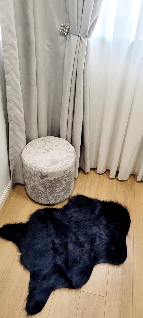 Une pièce avec un pouf rond, un tapis noir à poils longs et des rideaux beige.