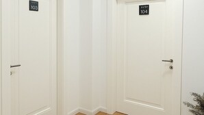 A hallway with two white doors, each marked with a number. A round, textured rug is placed on the floor. - Capital Inn Tirana (Tirana)