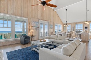 A spacious living room with a large window overlooking the ocean, a ceiling fan, and a dining area with natural light.