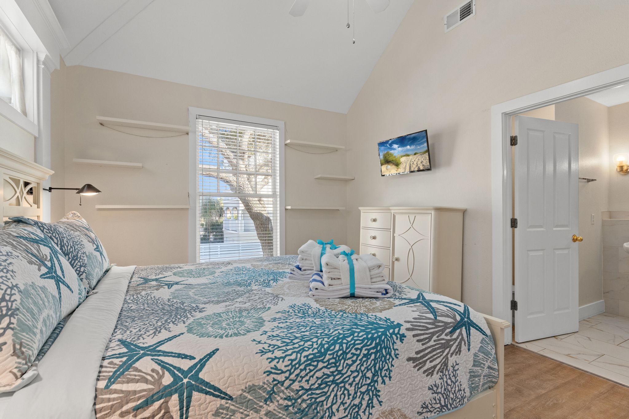 A bedroom with a bed, a nightstand, a dresser, a painting, and a door leading to a bathroom.