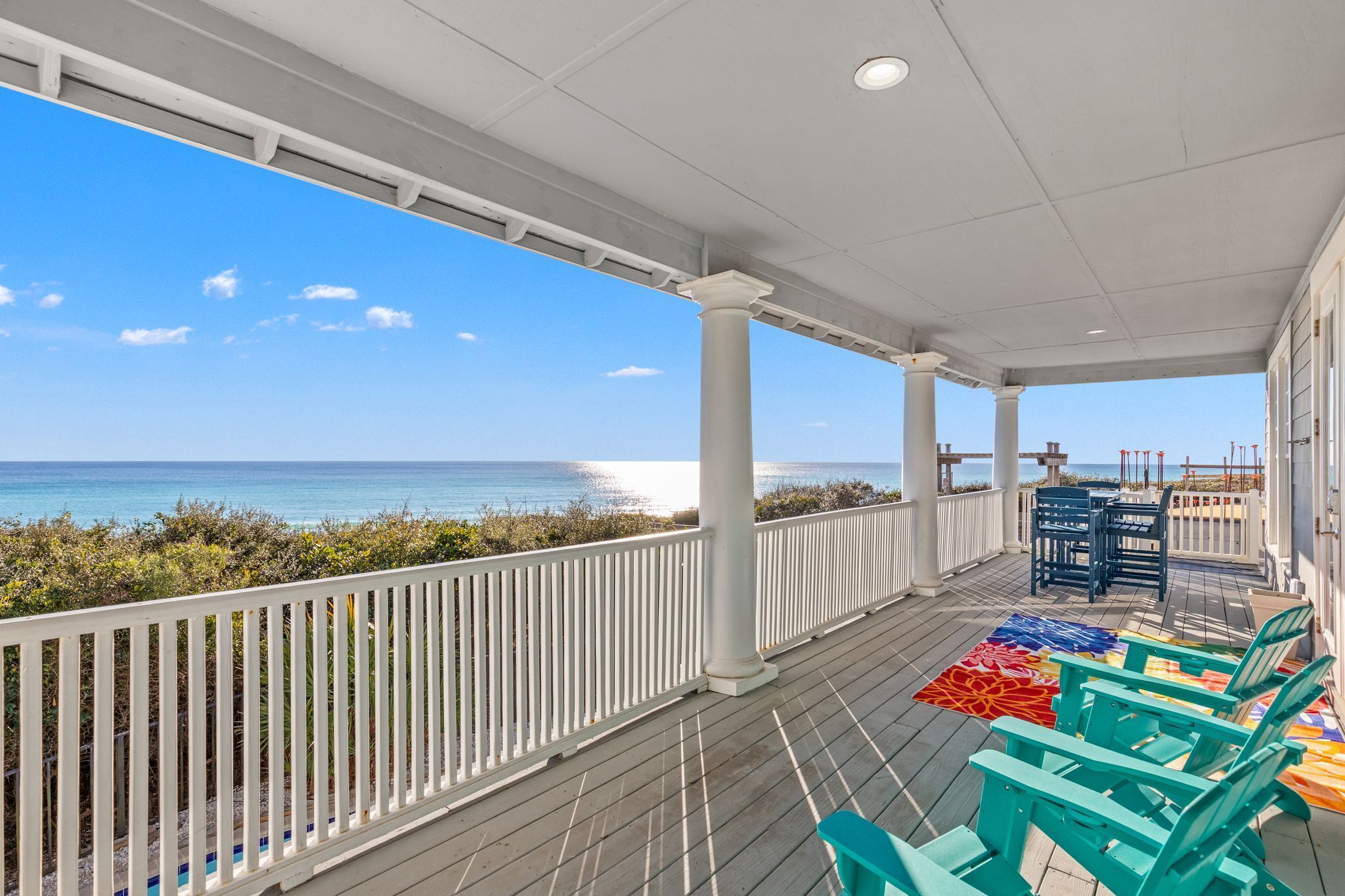 A covered outdoor area with a view of the ocean, white railings, and colorful outdoor furniture.