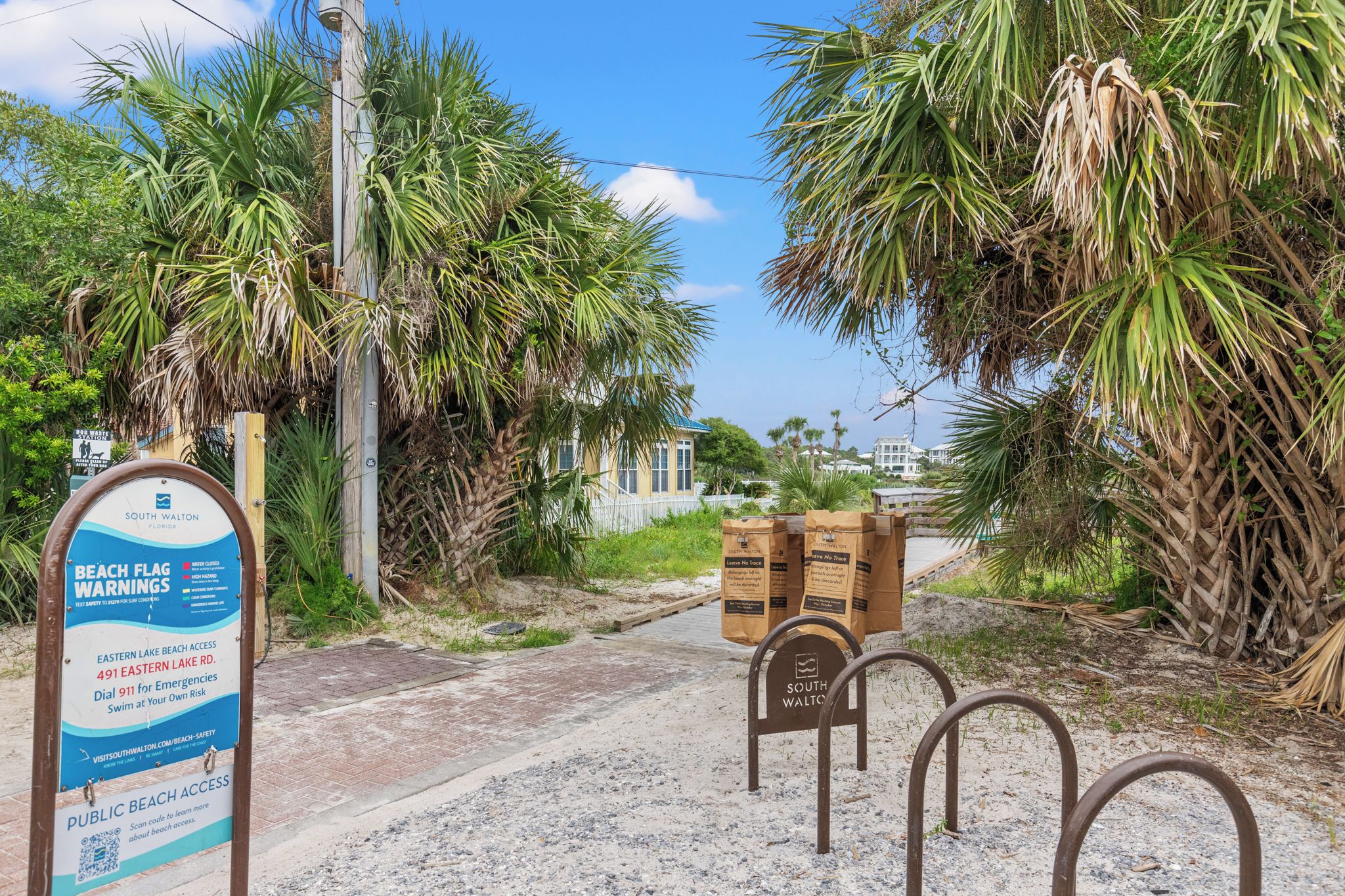 Un panneau indiquant l’accès à la plage et fournissant des informations sur l’accès public à la plage, un poteau indicateur en bois et une barrière métallique.