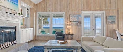 A living room with a fireplace, a large window with a view, a ceiling fan, and a blue rug.