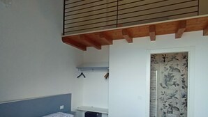 A bedroom with a large bed, a wooden ceiling, and a bathroom with floral tiles. - "Iseo" room (Marone)