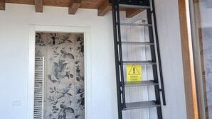 A modern bathroom with a wooden ceiling, a black metal ladder, a white sink, and a floral-patterned wall. - "Iseo" room (Marone)