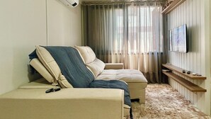 A room with a sofa, a television mounted on the wall, and a window with curtains.