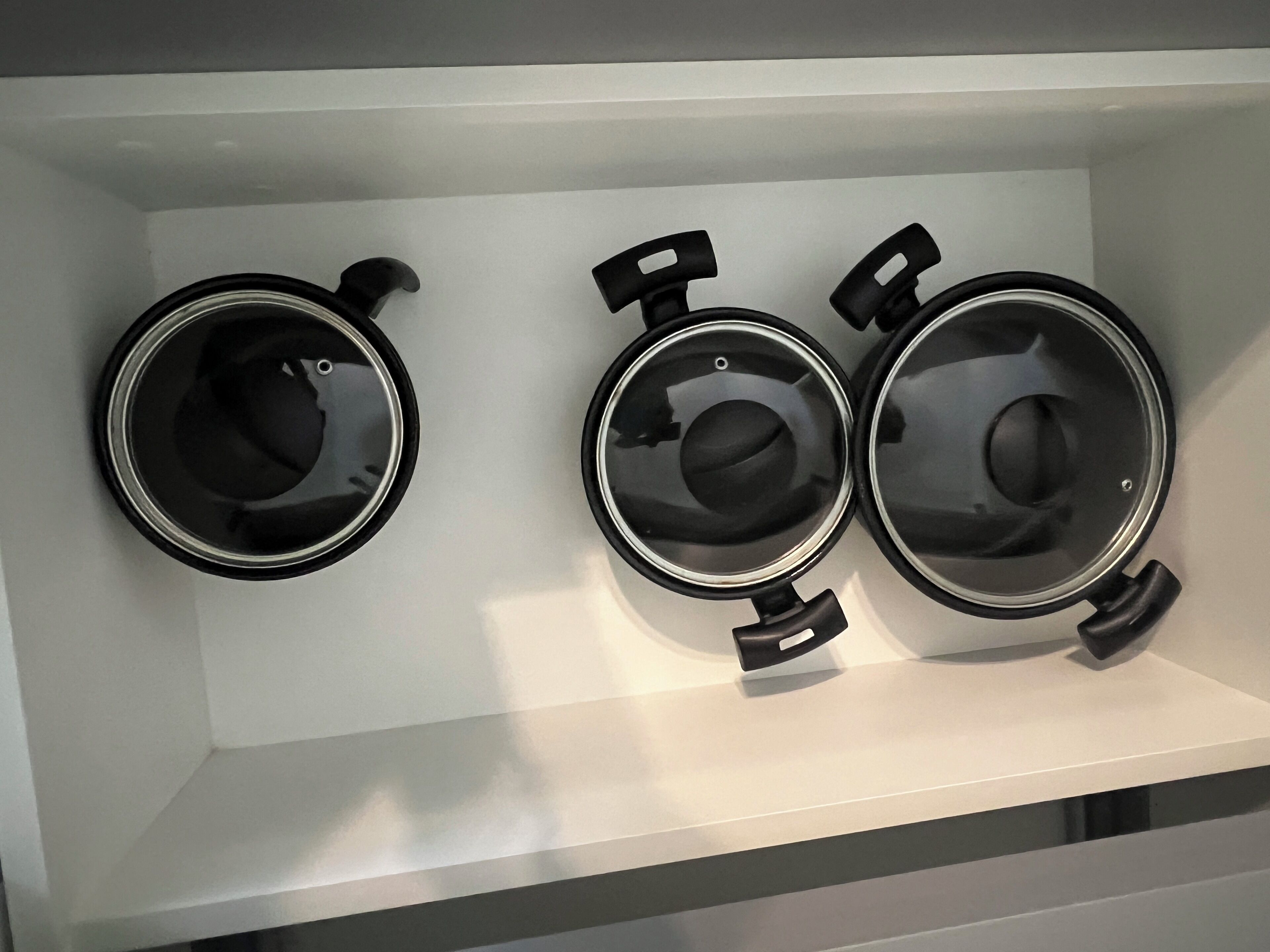 Trois pots noirs avec couvercles, posés sur une étagère blanche.