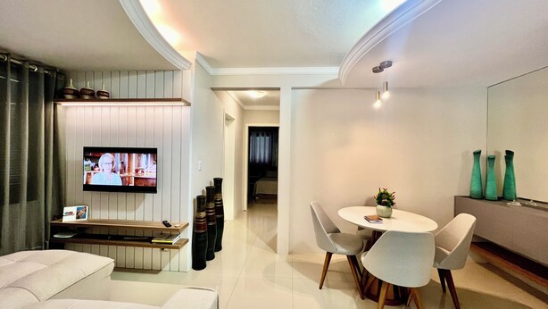 A modern living room with a flat-screen TV, a sofa, a dining table with chairs, and a small plant on the table.
