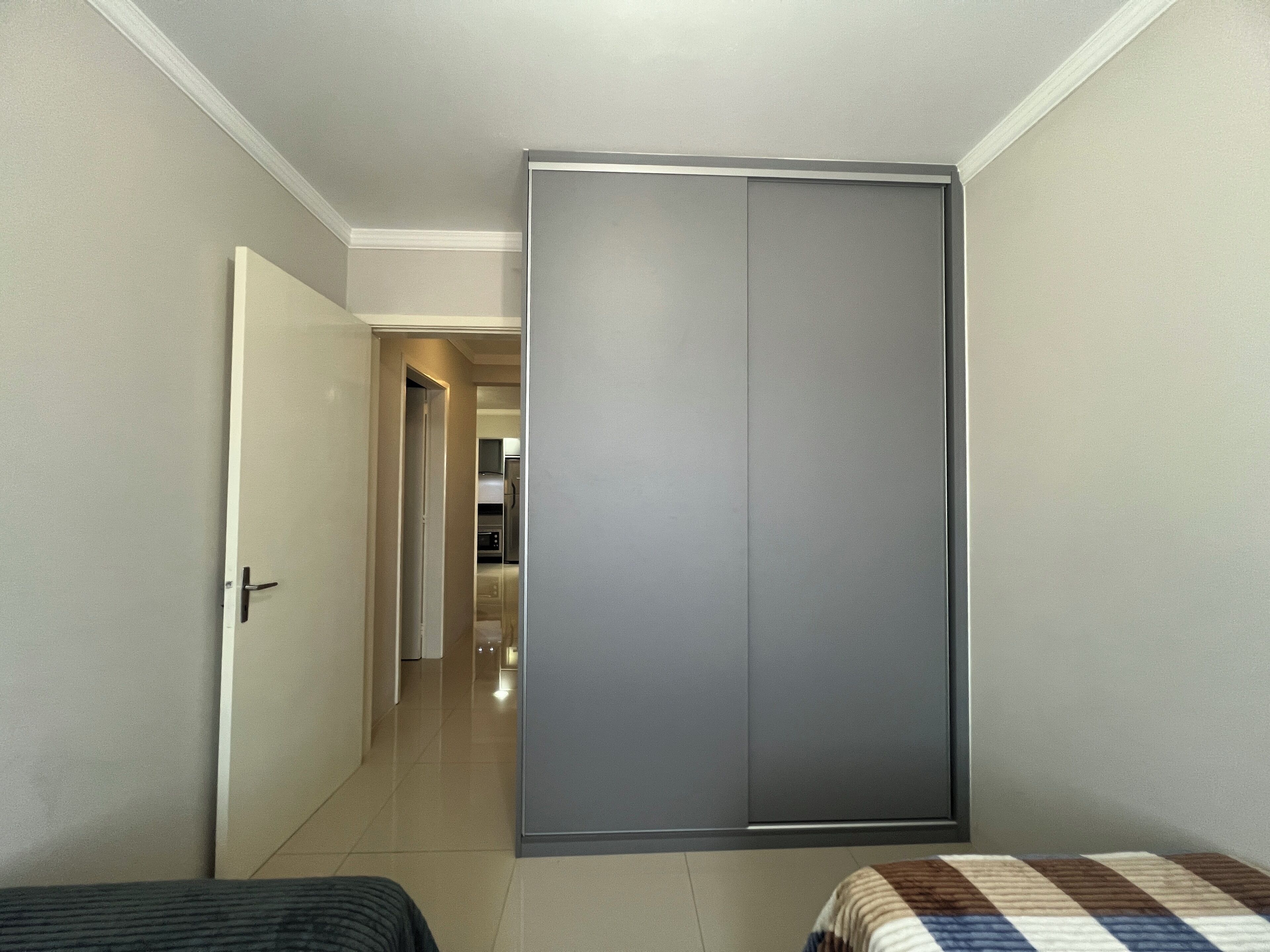 A bedroom with a wardrobe, a bed, and a view into the kitchen.