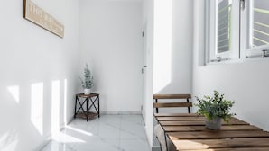 Una habitación luminosa y minimalista con un banco de madera, una mesita con una planta en maceta y un letrero en la pared.