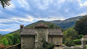 Ein Gebäude aus Stein mit einem Ziegeldach, umgeben von Grün und Bergen.
