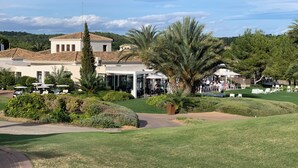 A large building with a white facade and a tiled roof, surrounded by well-maintained lawns and palm trees.