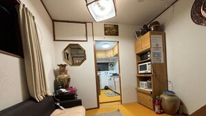 Un espacio habitable compacto con un sofá, una mesita, un florero decorativo y una cocina visible a través de un vano abierto.