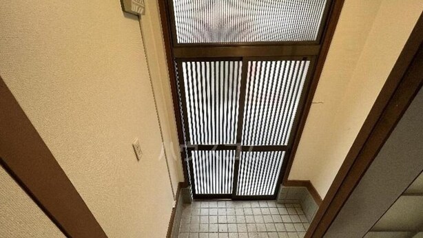 Un pasillo estrecho con suelo de baldosas y una puerta con persianas verticales.