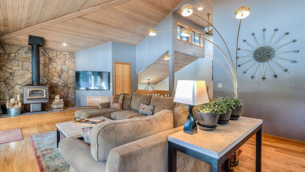 A cozy living room with a stone fireplace, a large sofa, a coffee table, and a modern lamp. - Relaxing 4BR Sunriver Retreat,Golf Views, Hot Tub, SHARC Passes, Game Room (Sunriver)