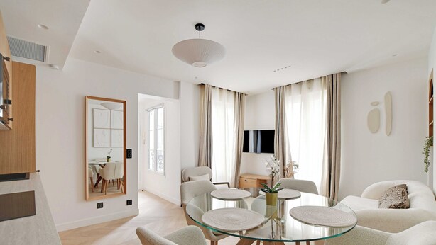 A modern living room with a glass dining table, comfortable seating, a flat-screen TV, and a large mirror. - Charming Apartment - AC- 3br-6p- Montorgueil (Paris)