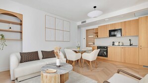 A modern living room with a sofa, coffee table, and chairs, a kitchen with wooden cabinets and appliances, and a dining area with a glass table. - Charming Apartment - AC- 3br-6p- Montorgueil (Paris)