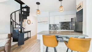 Una cocina moderna con una isla central, armarios blancos y una escalera espiral negra.