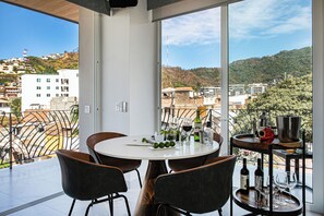 A balcony with a round table, chairs, and a view of the city and hills.