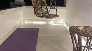 A room with a hanging rattan chair, a purple exercise mat, and a wicker table.