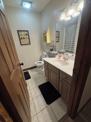 A bathroom with a toilet, sink, and mirror. There is a towel rack and a framed picture on the wall.