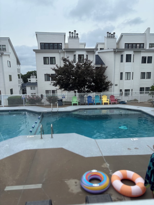 A swimming pool with a white fence and colorful chairs, surrounded by white buildings.