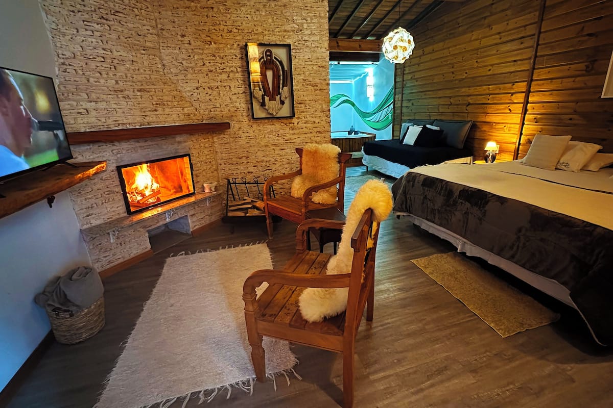 Ein gemütliches Zimmer mit Kamin, einem Bett, einem Fernseher und einem großen Fenster.