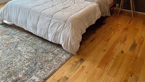 A bedroom with a large bed, two bedside tables with lamps, a rug, and a brick wall. - Market street apartment (Corning)