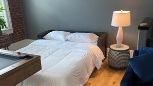 A bedroom with two beds, a bedside table, a lamp, and a blue sofa. - Market street apartment (Corning)