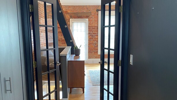 A hallway with wooden flooring leading to a room with a brick wall and a staircase. - Market street apartment (Corning)