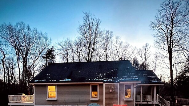A house with a fire pit in the yard, surrounded by Adirondack chairs.