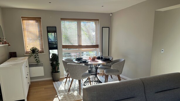 Un salon moderne avec un canapé gris, un coin repas comprenant une table ronde et des chaises, et un meuble blanc.