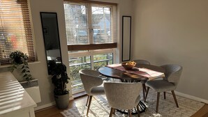 Un coin repas avec une table ronde, quatre chaises, un saladier de fruits et une vue dégagée sur l’extérieur grâce à de grandes fenêtres.