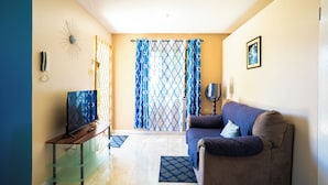 A living room with a TV on a stand, a sofa, and a patterned curtain. - Cozy 1-bedroom apartment in charming Mandeville with WiFi, AC (Mandeville)
