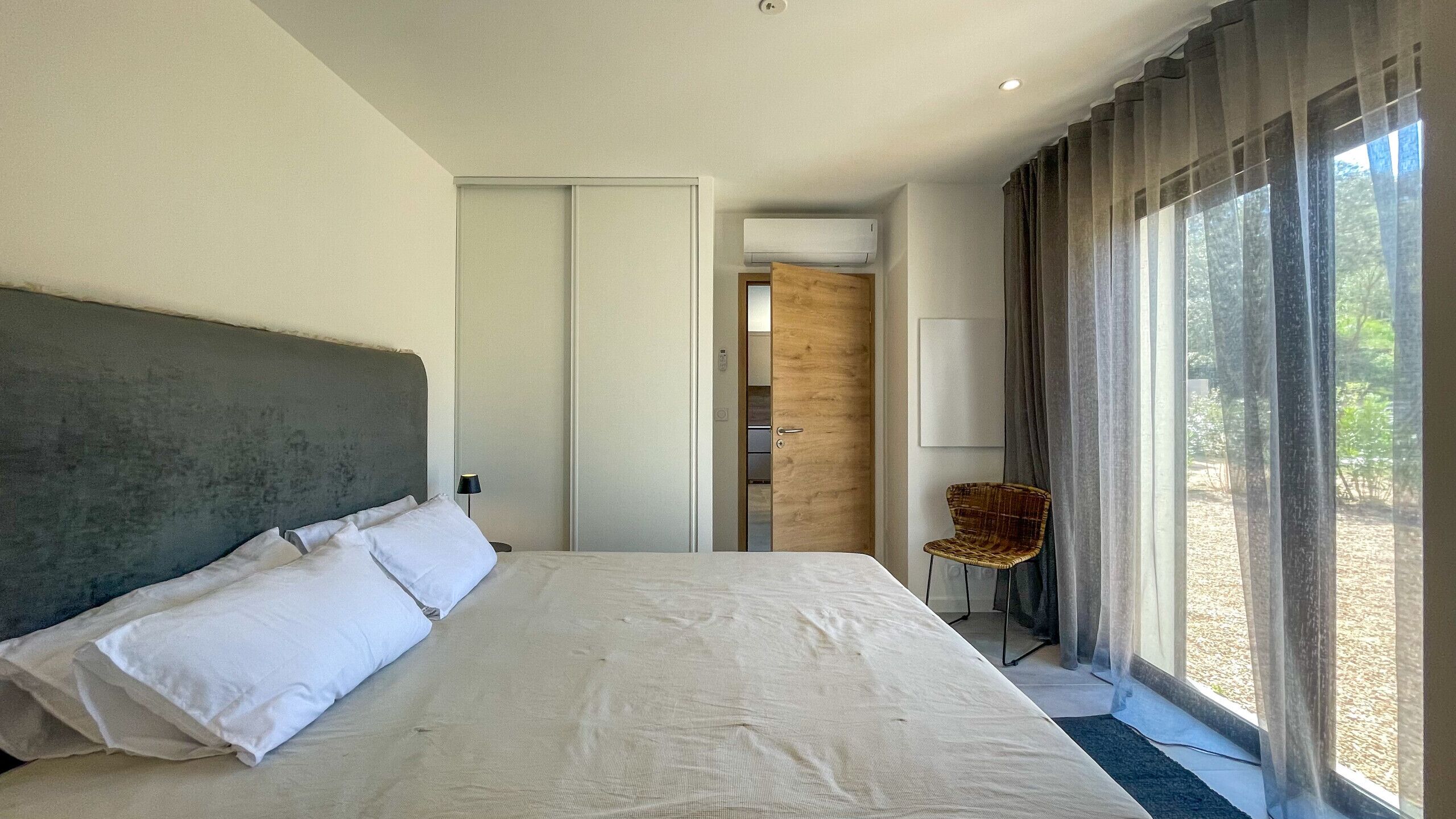 Une chambre d’hôtel moderne avec un grand lit, une porte en bois, une chaise et une vue sur l’extérieur.