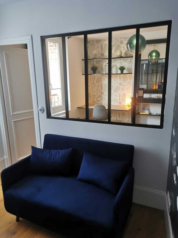 A room with a dark blue sofa, a window with a black frame, and a wall with patterned wallpaper. - Le Beluga Apartment - Near the Sea - Downtown Veules-Les-Roses (Veules-les-Roses)