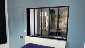 A bedroom with a bed, a window with a black frame, and a wall-mounted lamp. - Apartment le Beluga - near the sea - center of Veules-Les-Roses (Veules-les-Roses)