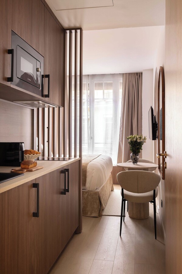 A compact hotel room with a kitchenette, a bed, a seating area, and a view of the city. - Charming Studio - 2P- Madeleine (Paris)