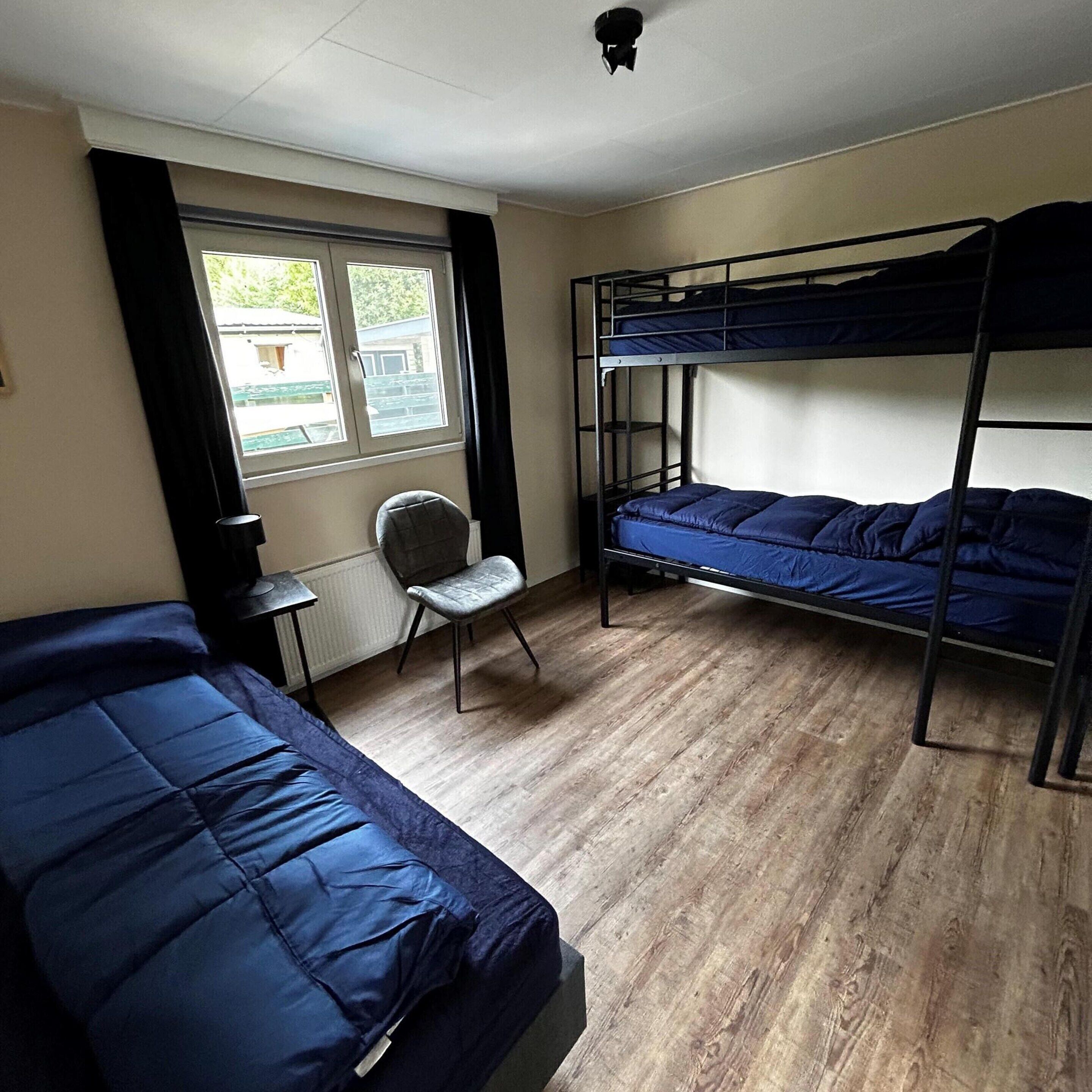 Un dormitorio con literas, una silla y un ventanal.