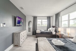 Ein modernes Schlafzimmer mit Bett, Nachttischen, einem Schminktisch, einem Fernseher und einem Fenster mit Vorhängen.