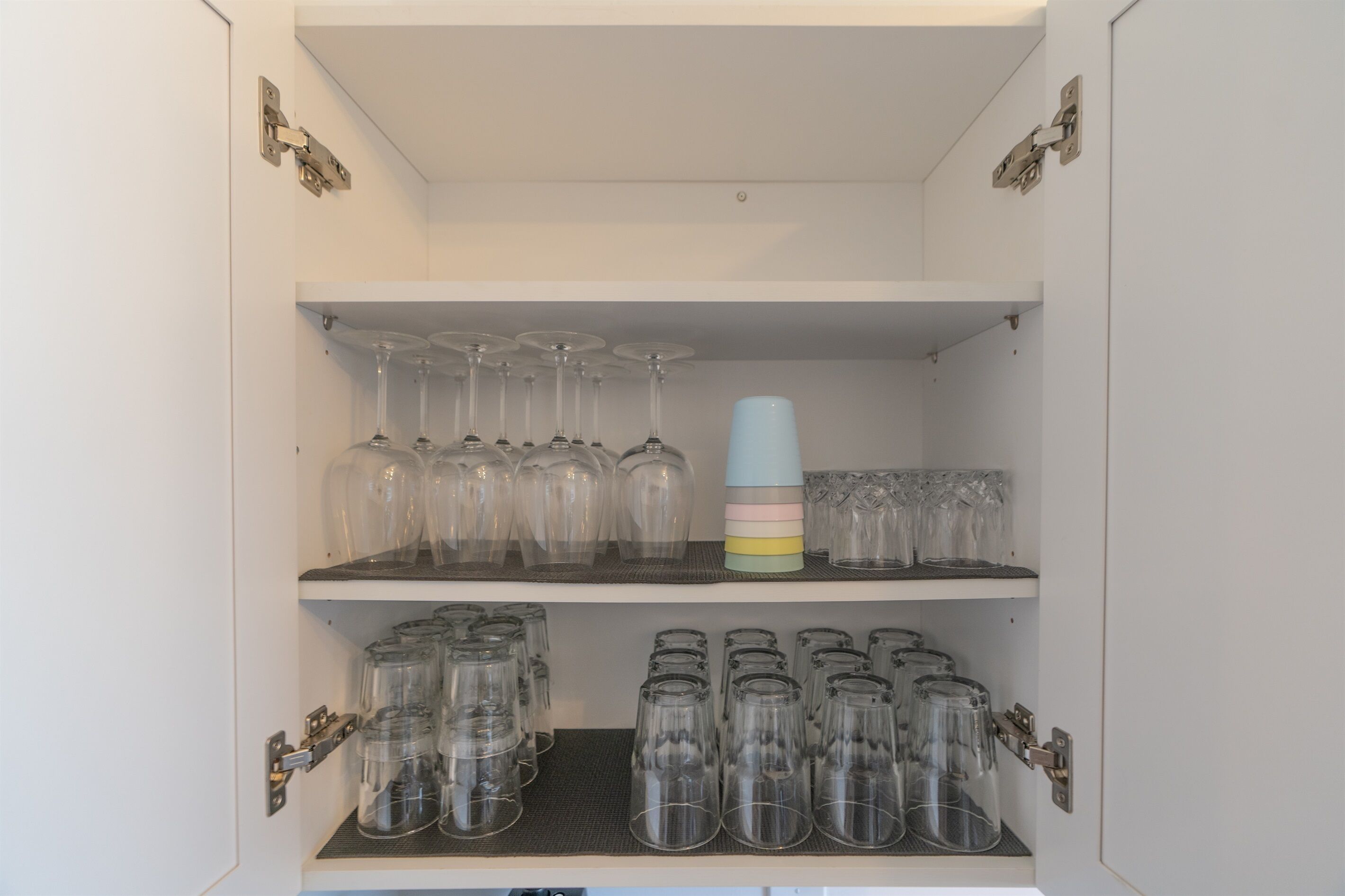 A storage cabinet with shelves containing clear glassware and a stack of colorful cups.