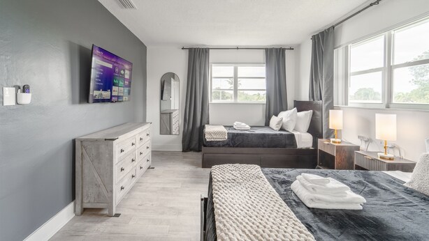 Um quarto moderno com cama, mesas de cabeceira, cômoda, televisão e janela com cortinas.
