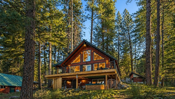 Eine zweigeschossige Holzjagdhaus mit einem Balkon, umgeben von hohen Kiefern.