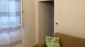 A living room with a brown sofa, a floral pillow, a window with a striped curtain, and an air conditioning unit on the wall.
