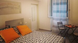 A bedroom with a bed, a chair, a small table, and a window with a curtain.