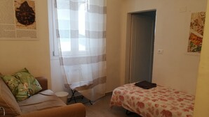 A small, cozy room with a single bed, a sofa, and a window with a curtain.